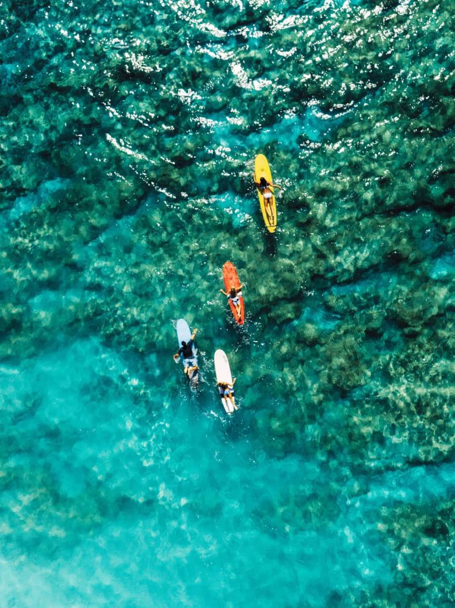 aerial view of four surfers with colorful surfboards in hawaii