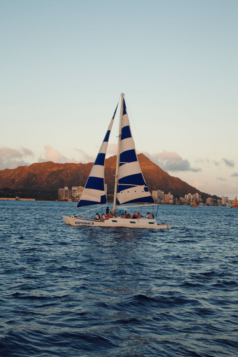 sailboat at dusk going past the famous diamond head peak in oahu hawaii