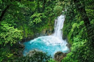bright blue waterfall surrounded by green jungle in costa rica, epic honeymoon destination for december