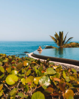 girl sitting at the edge of infinity pool with green plants in the foreground