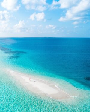 remote island in the ocean with blue water and single person standing on white sand beach
