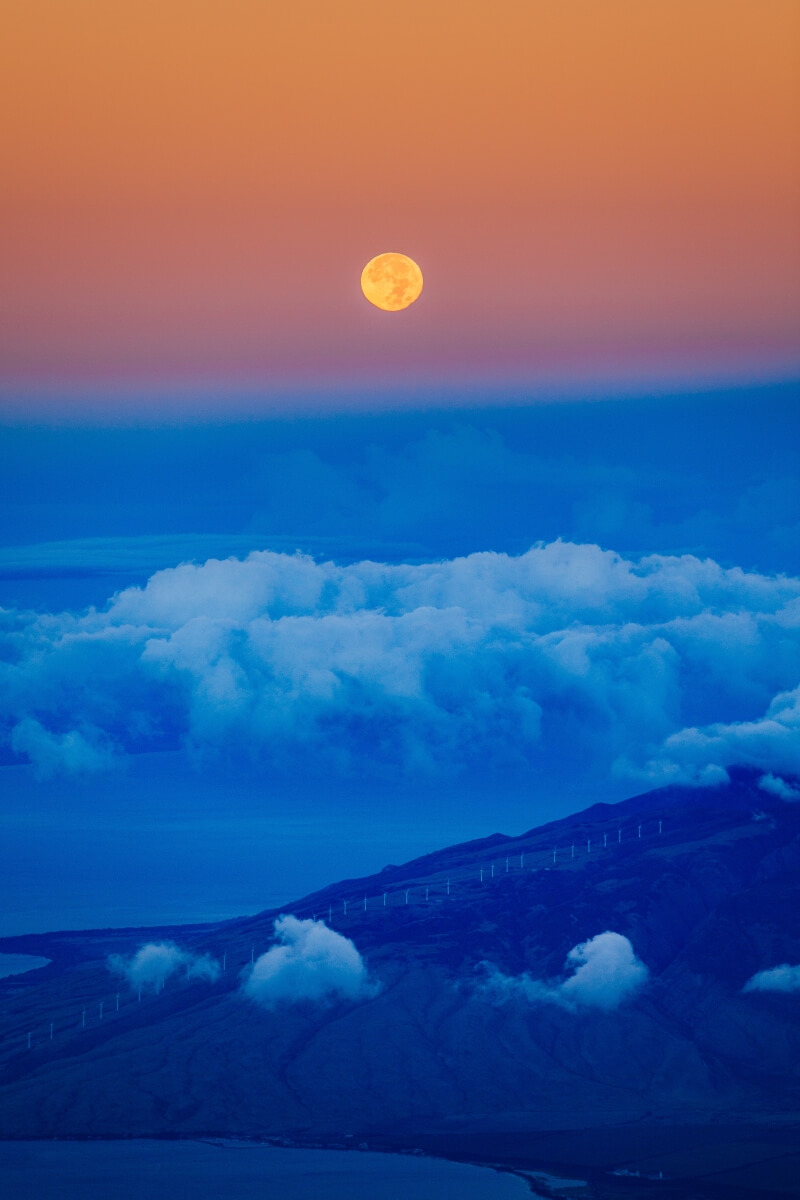 moon rises over haleakala national park in maui hawaii with contrasting orange and blue colors