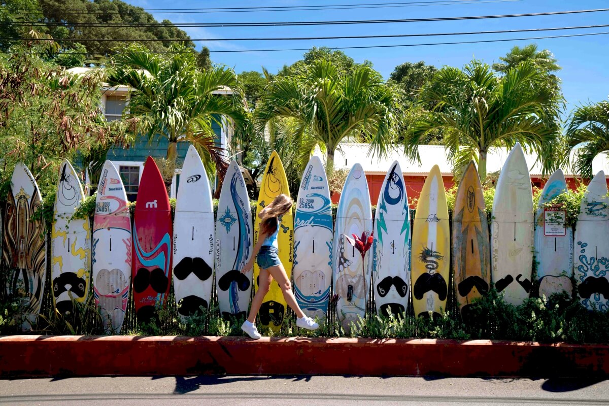 girl walking along wall made up of colorful surfboards in hawaii