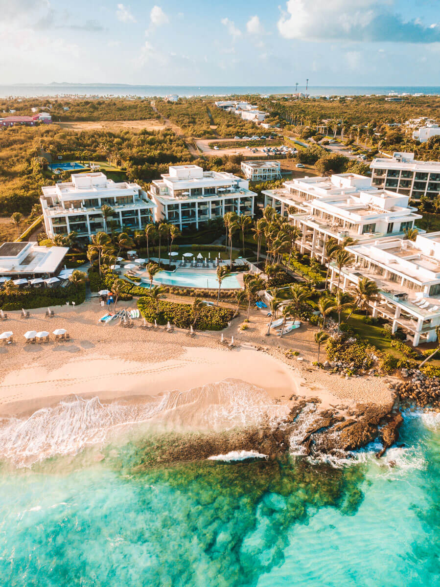 drone view of buildings right up against white sand beach and turquoise waters