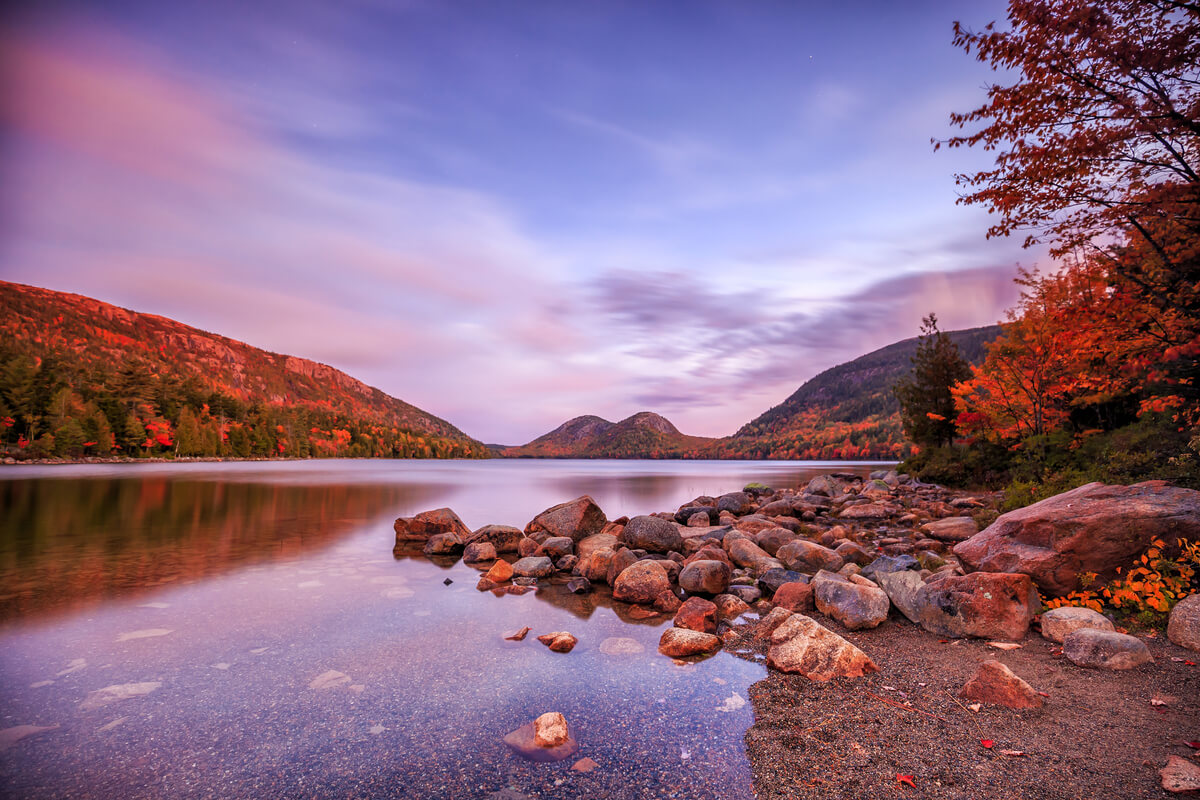 sunset over lake in acadia national park during fall with fall leaves covering the trees surrounding the lake
