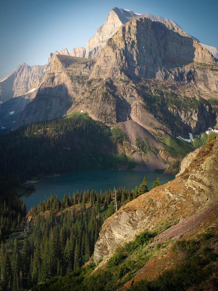 mountainous landscape with lake in the middle surrounded by trees in glacier national park in montana