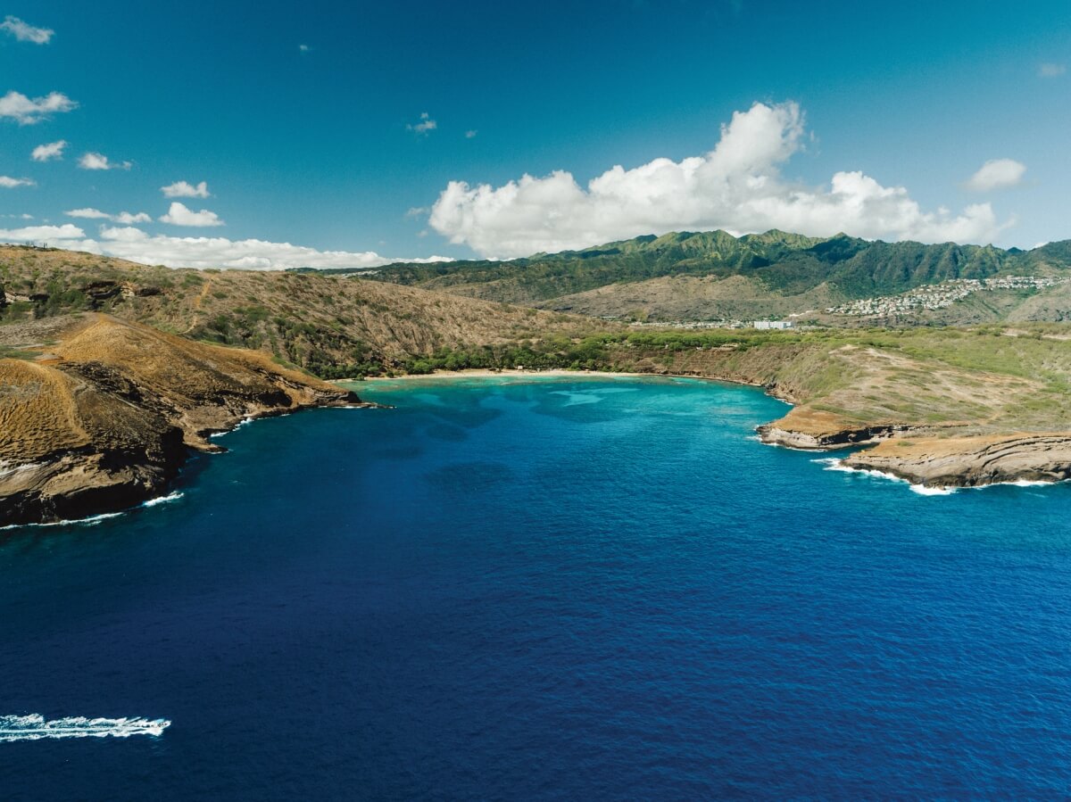aerial view of Hanauma Bay in Oahu, which is a cove beach area, with green mountains in the background and the turquoise waters in the foreground