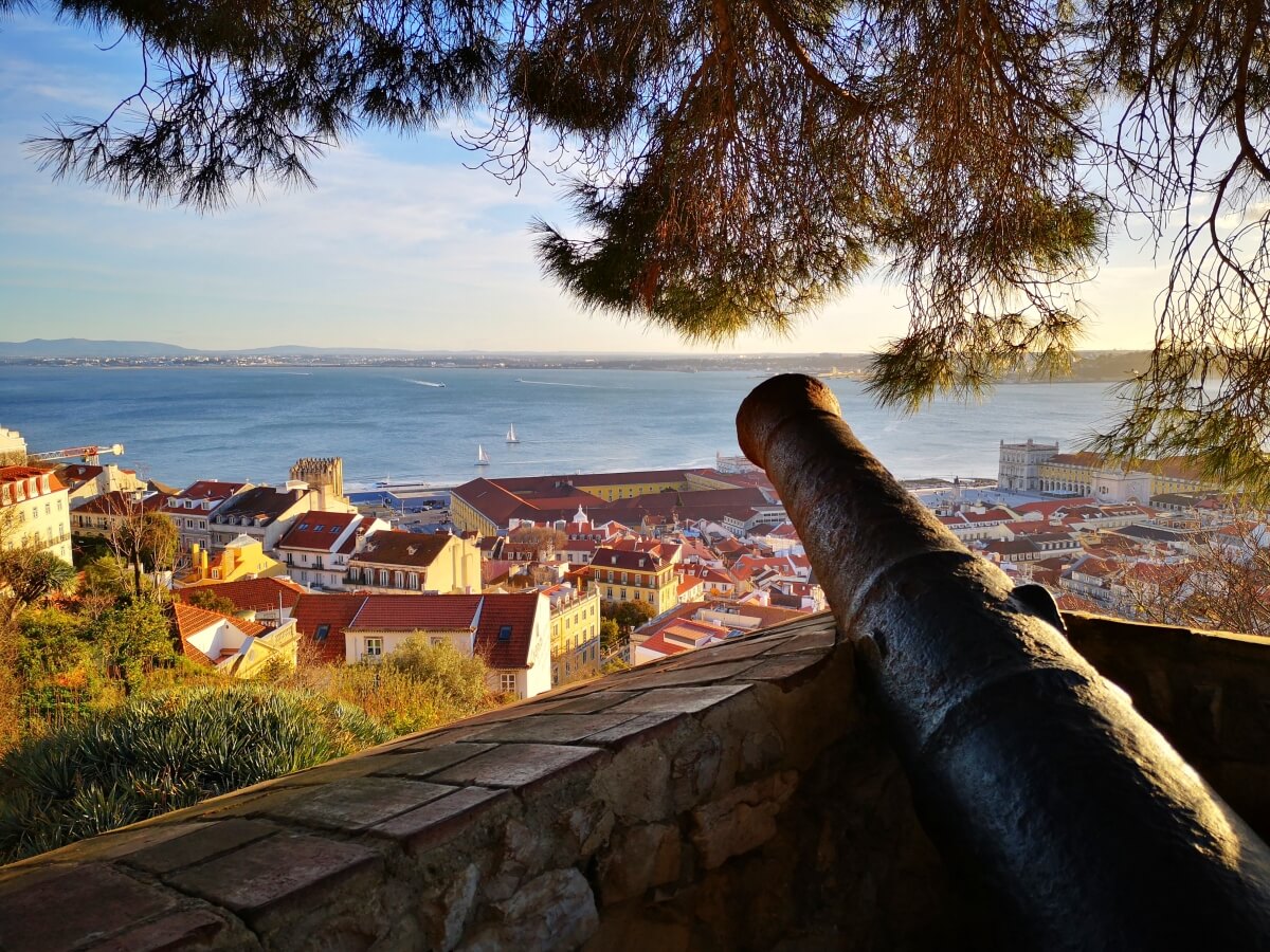 view point in lisbon with canon pushing through stone wall overlooking the city with orange rooftops next to the water
