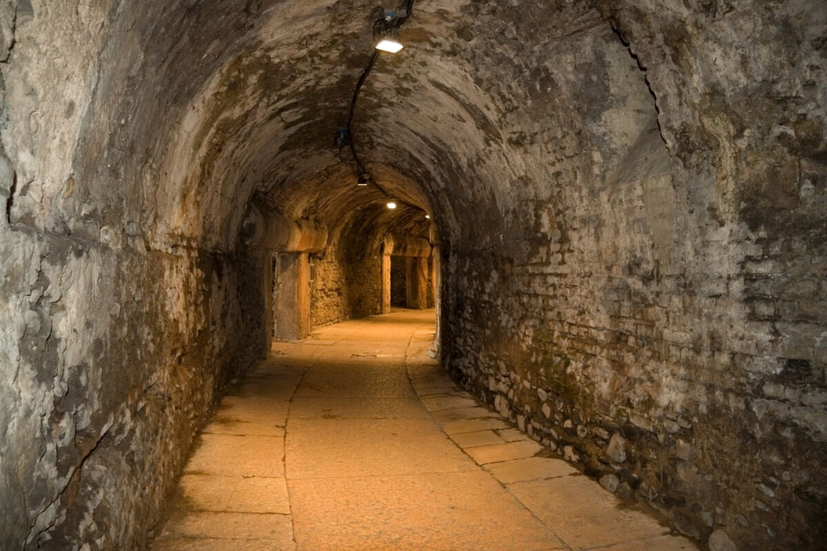 a dimly lit, winding hallway in the catacombs with walls of stone