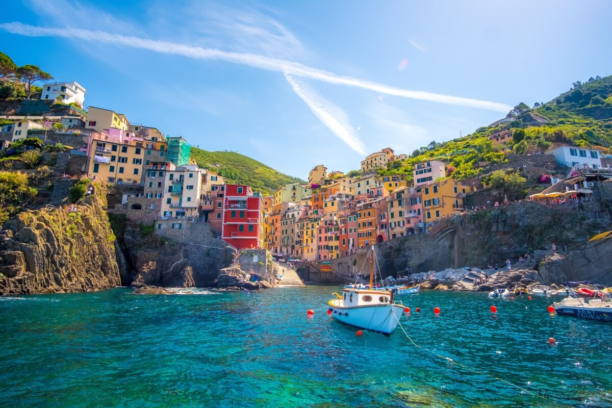 a view from the water of a colorful town in italy's cinque terre with a boat in front of it