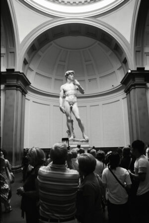 black and white photo of tourists taking photos of the famous david statue by michelangelo at accadmia gallery in florence italy