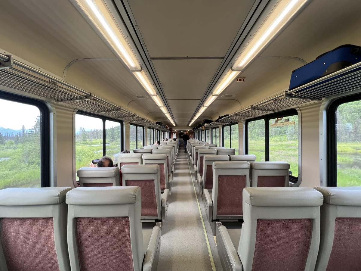 back of seats on alaska railroad's adventure class showing bag storage area above seats with alaska landscapes in view out the windows on either side of the aisle
