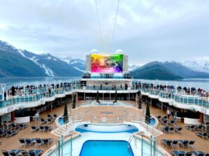 alaska cruise ship deck with pool and colorful jumbo screen surrounded by alaska glaciers and mountains on a beautiful sunny day