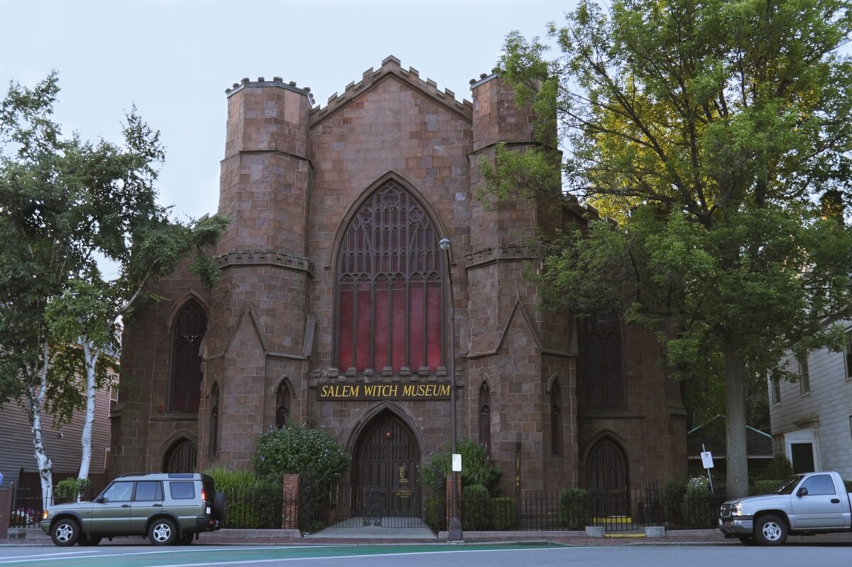 the salem witch museum, a brick building built to look like a castle, with 2 cars parked in front of it 