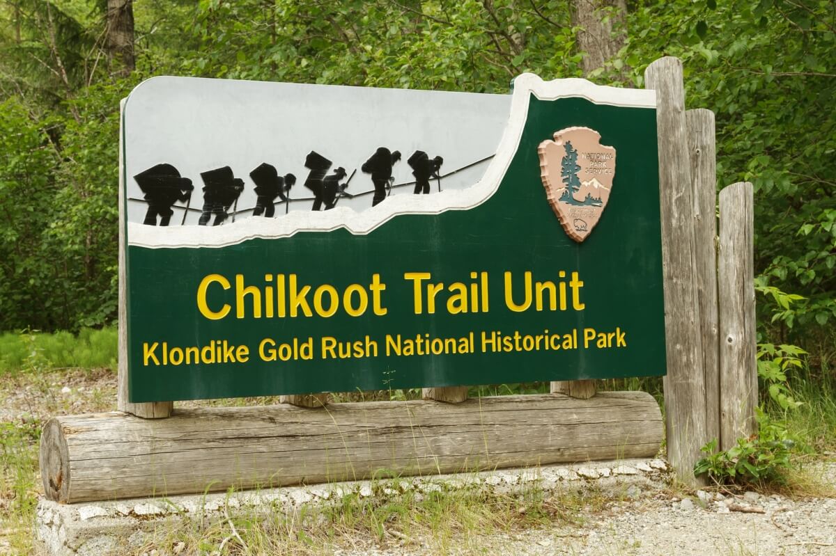 sign for the chilkoot trail unit in the klondike gold rush national historical park with nps symbol and black and white image of people hiking