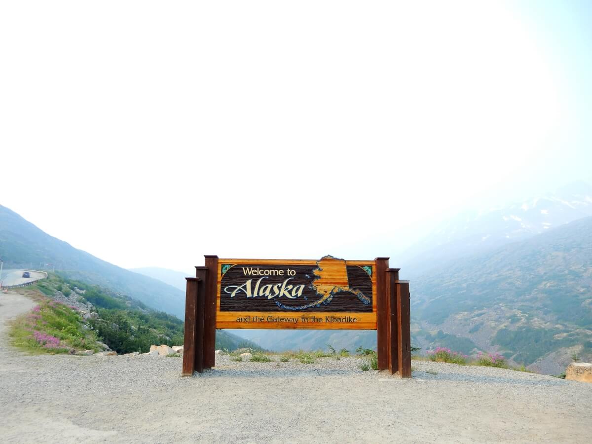 welcome to alaska wooden state sign in front of valley of mountains