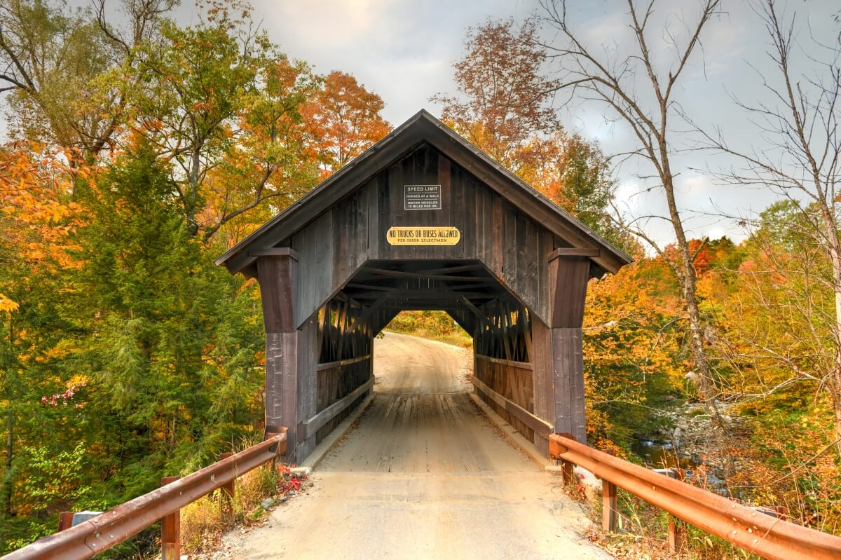 Gold Brook Covered Bridge in Stowe, VT, also known as Emily's Bridge - a dark wooden covered housing over a dirt road bridge surrounded by colorful fall foliage