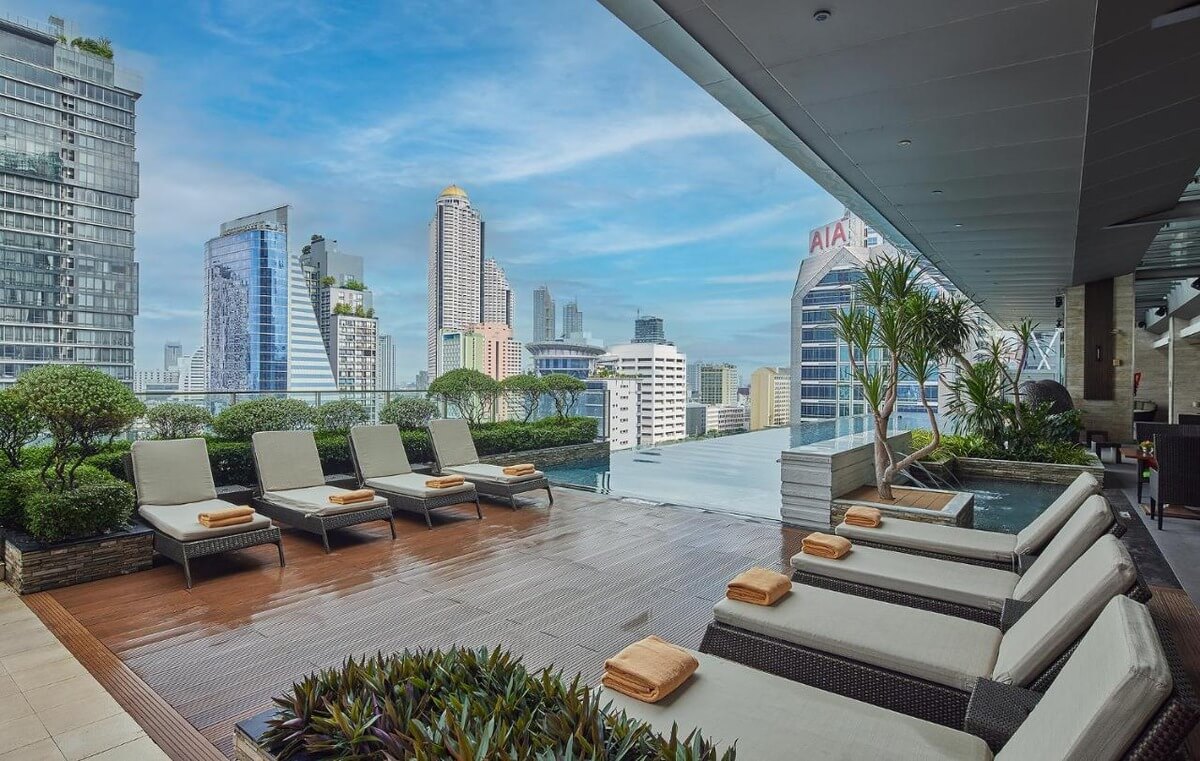 infinity pool at the Eastin Grand Hotel Sathorn in Bangkok with 8 lounge chairs and orange towels overlooking the Bangkok skyline