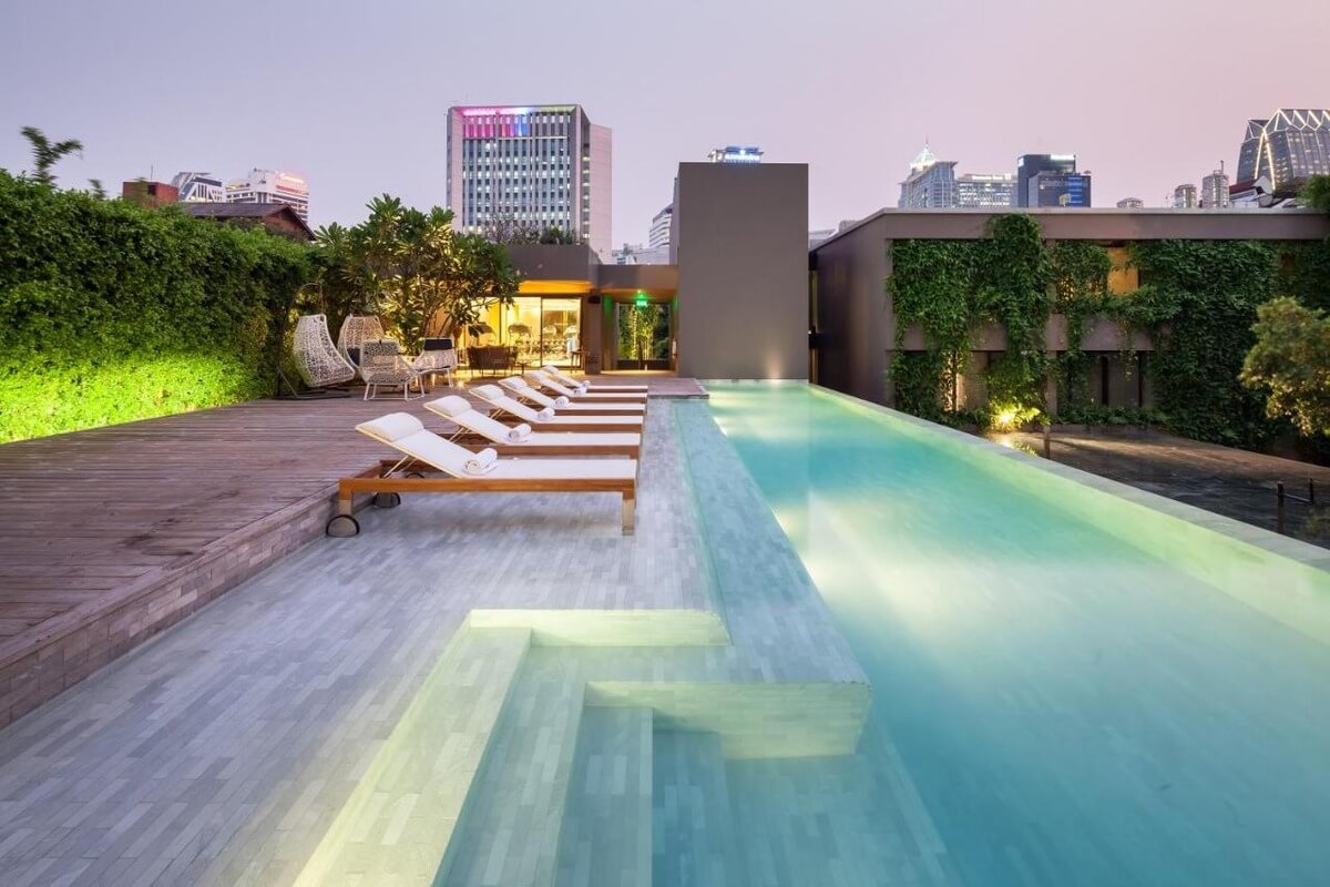 side vide of a low rooftop pool at Ad Lib Hotel in Bangkok with pool chairs in a shallow part of the pool at dusk