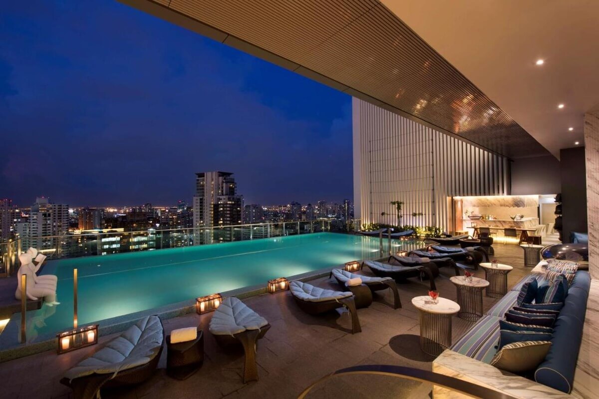 lounge area at the Hilton Sukhumvit Bangkok hotel with lounge chairs that look like leaves next to the hotel's infinity pool lit up at night