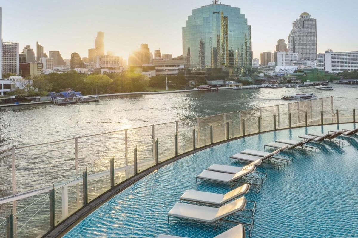 circular infinity pool at the Hilton Millennium in Bangkok with several pairs of lounge chairs in the shallow depths of the pool overlooking the Chao Phraya River