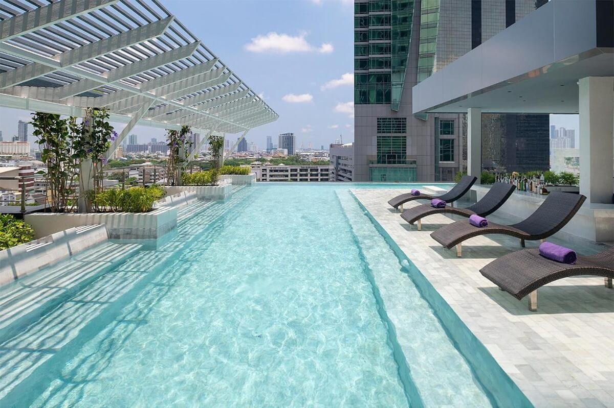 infinity pool at the Mode Sathorn Hotel with black chairs and purple towels and shaded by a partial roof and surrounded by plants