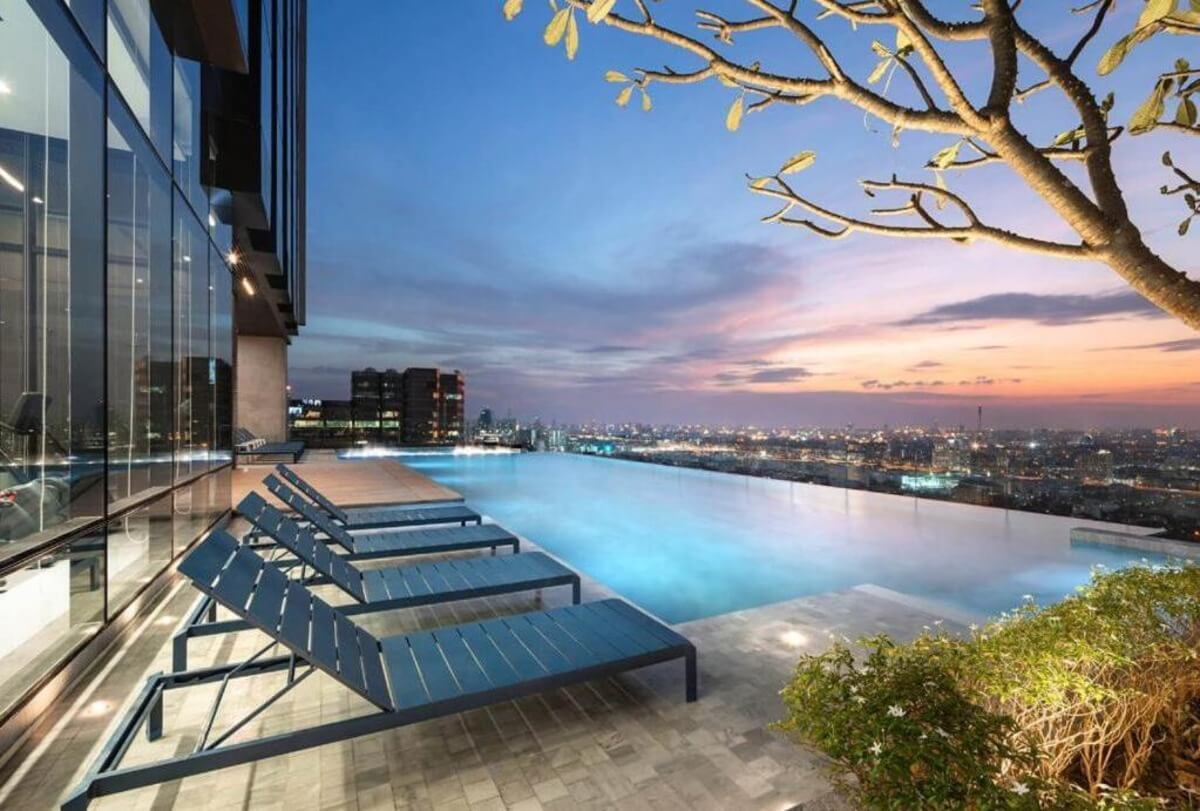the sun setting over the Bangkok skyline in the background of the lit up infinity pool at the Quarter Ari hotel