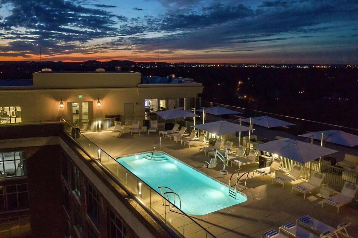 an aerial view of the rooftop pool at the Hilton in Nashville's Green Hills neighborhood lit up at night with umbrellas and pool chairs surrounding the pool