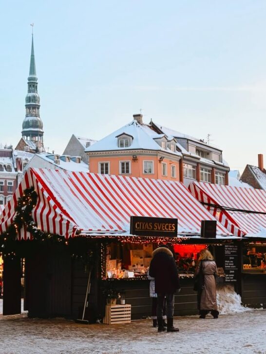 Christmas Market in Riga, Lativa set up in city's Dome Square, with festively decorated stalls with red and white striped roofs and colorful European buildings in the background