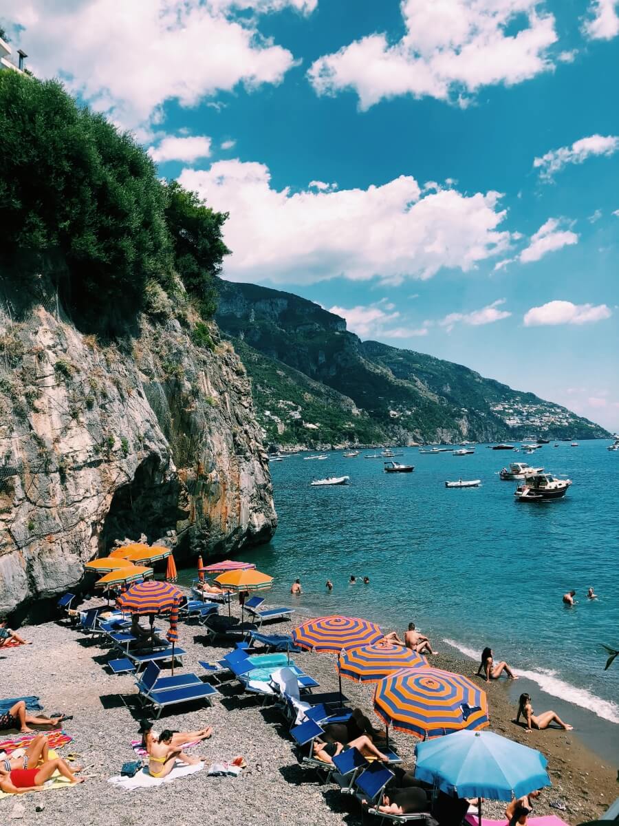 orange and blue umbrellas and chairs set up on a rocky beach next to the ocean in Positano, Italy