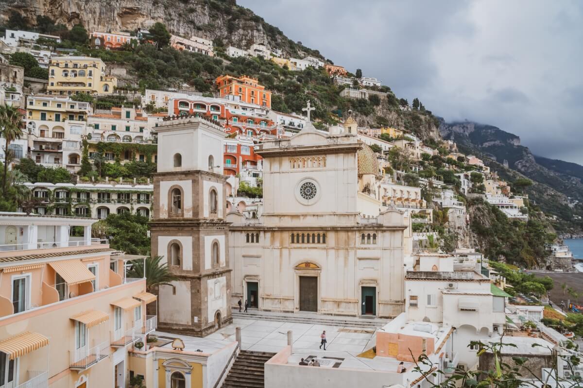 the simple looking church of santa maria assunta sitting amongst colorful buildings in the town of Positano Italy