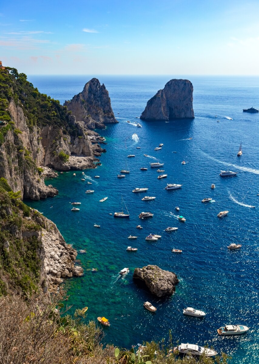 aerial view of lots of boats in the ocean next to the cliffs in Capri Italy