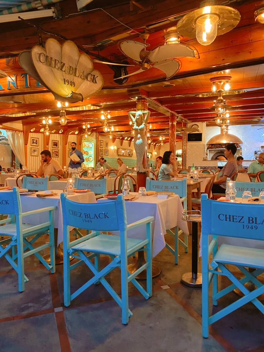blue chairs at a restaurant with the restaurant name, Chez Black, on them in front of the rest of the restaurant in Positano