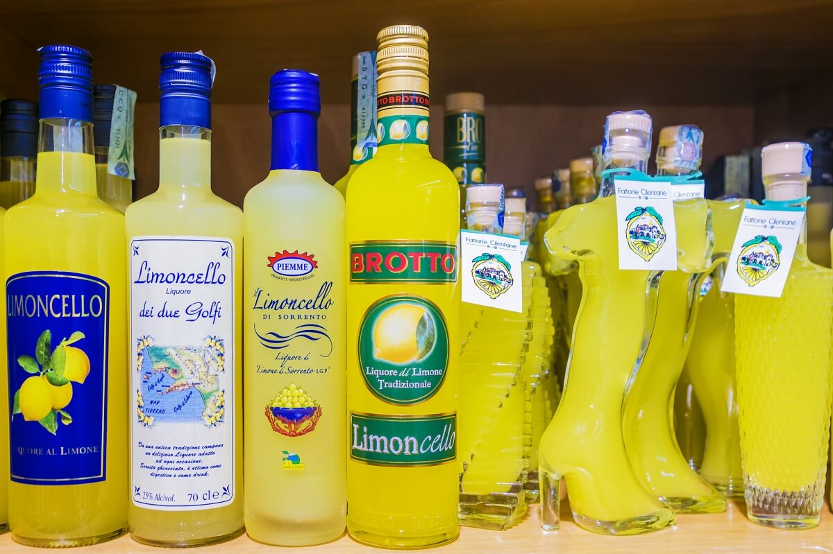 close up photo of several bottles of limoncello from different companies - some of which are shaped like the country of Italy