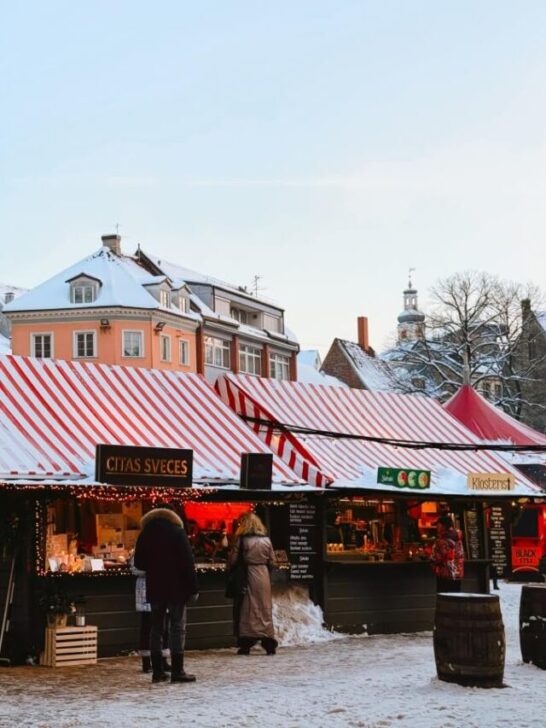 Christmas Market in Riga, Lativa set up in city's Dome Square, with festively decorated stalls with red and white striped roofs and colorful European buildings in the background